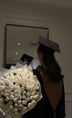 a woman wearing a graduation cap and gown holding a bouquet of flowers in front of a mirror