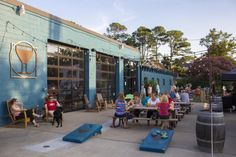 several people sitting at picnic tables in front of a blue building with beer kegs