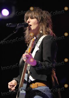 a woman singing into a microphone and holding a guitar in her hand at a concert