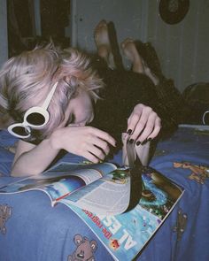 a woman laying on top of a bed next to a book and pair of sunglasses