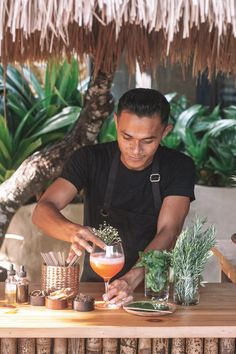 a man in black shirt making drinks at a table with plants and potted plants