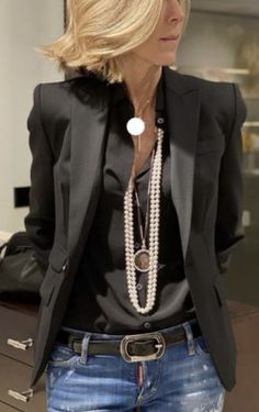 a woman wearing a black blazer and jeans is standing in front of a mirror