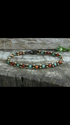 a beaded bracelet with gold and green beads on top of a piece of wood