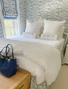 a white bed sitting next to a window in a room with blue and white wallpaper