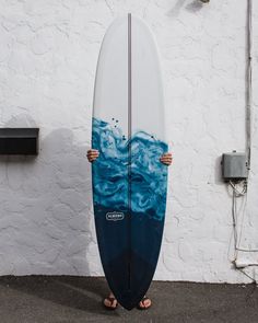 a person standing in front of a white wall holding a surfboard with blue waves painted on it