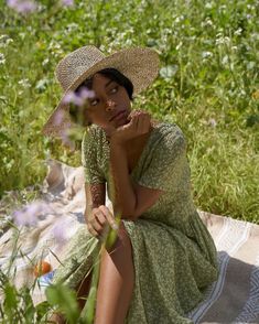 a woman wearing a hat sitting on a blanket in the middle of a field with wildflowers