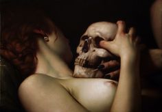 a woman is holding a skull in her hand and looking down at the skeleton on her chest