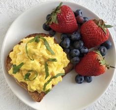 an egg salad on toast with strawberries and blueberries is served on a white plate