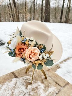 a white hat with flowers and feathers sitting on top of a stand in the snow