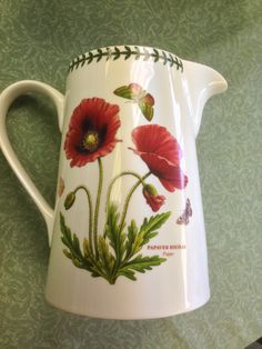 a white pitcher with red flowers painted on it's side and green leaves around the rim