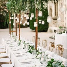a long table with white linens and greenery is set up for an outdoor dinner
