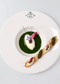 a white plate topped with two small appetizers on top of green sauce and garnish