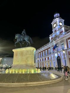 people are walking around in front of a building with a clock tower and horse statue