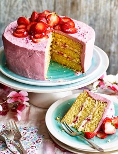 there is a cake with pink frosting and strawberries on the plate next to it