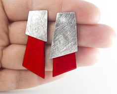 a pair of red and silver earrings in someone's hand on a white background