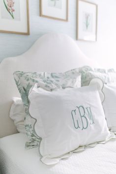 two pillows on top of a bed with white sheets and green trimmings, in front of framed pictures