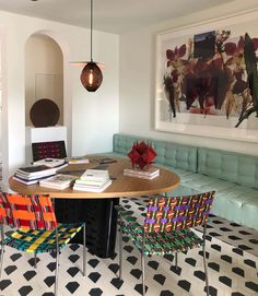 a dining room table with colorful chairs and artwork on the wall above it, along with two couches