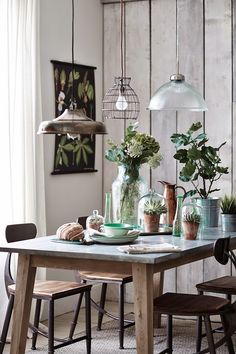 a dining room table with plants in vases and hanging lights over the top of it