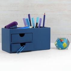 a blue drawer with pens and pencils in it next to a small glass vase