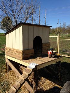 a dog house built into the side of a fenced in area with hay on the ground