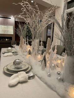 the table is set with silver and white christmas decorations, candles, and snow - covered trees