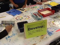 several people sitting at a table with paint and paper on it that says develop