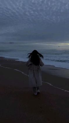 a woman is walking on the beach at night with her back to the camera, looking out into the ocean