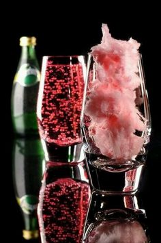 three glasses with pink cotton candy and two empty wine glasses next to each other on a reflective surface