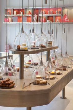 an assortment of desserts on display in a glass case with hanging lights above them