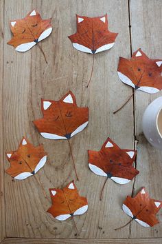 paper leaves are arranged in the shape of foxes on a wooden table next to a cup of coffee