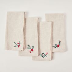 four embroidered linen napkins with holly and red berries on them, lined up against a white background
