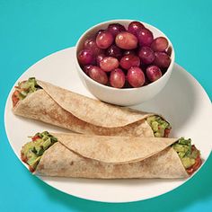 two burritos on a plate with grapes and guacamole in a bowl