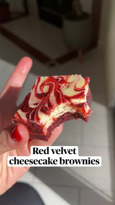 a hand holding a piece of red velvet cheesecake brownies with white swirls