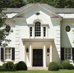 a large white house with black shutters on the front door and windows, surrounded by lush green grass
