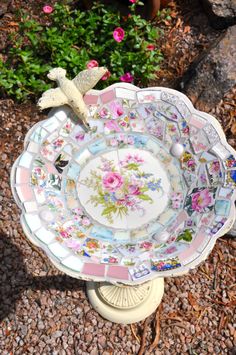 a birdbath sitting on top of a flowered plate in the middle of a garden