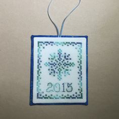 a cross stitch ornament hanging from a string on a white surface with blue trim