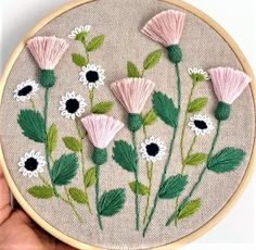 someone is holding up a embroidery project with pink and white flowers in the middle of it
