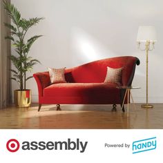 a red couch sitting on top of a hard wood floor next to a tall plant