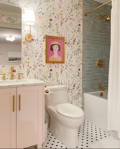 a white toilet sitting next to a bath tub in a bathroom under a painting on the wall
