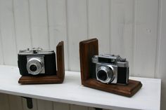 two old fashioned cameras sitting on top of a white shelf next to each other, one is black and the other is brown