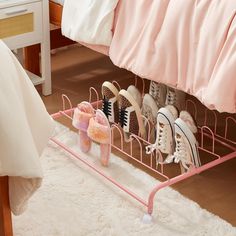 there is a pink rack with pairs of shoes on it in front of a bed