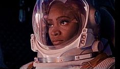 a woman in an astronaut's helmet looks into the distance with her eyes wide open