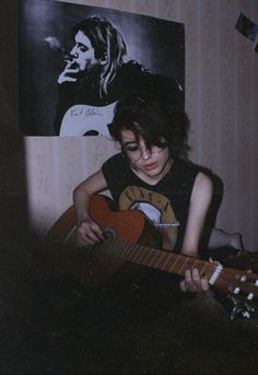 a young person playing an acoustic guitar in front of a wall with pictures on it