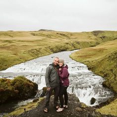 a man and woman standing on top of a hill next to a river in iceland