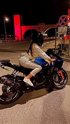 a woman riding on the back of a blue motorcycle at night in front of a red light