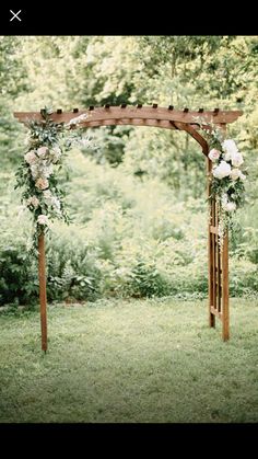 a wooden arbor with flowers and greenery on the grass in front of some trees