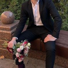 a man in a suit and tie sitting on a bench holding a bouquet with flowers