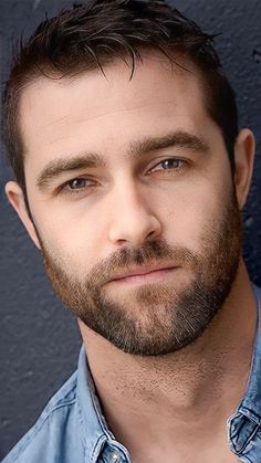 a close up of a person wearing a blue shirt and beard with a serious look on his face