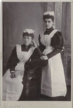 an old black and white photo of two women dressed in period clothing, standing next to each other