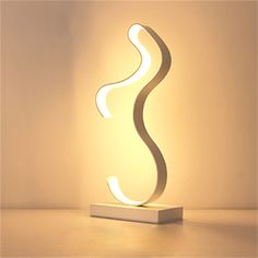a white lamp sitting on top of a table next to a light bulb in the shape of a wave